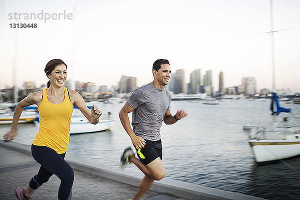 Glückliche männliche und weibliche Athleten joggen auf der Mole am Hafen