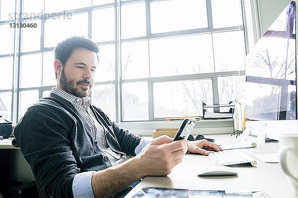 Geschäftsmann benutzt ein Smartphone  während er im Büro am Schreibtisch sitzt