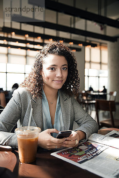 Porträt einer Geschäftsfrau  die ein Smartphone am Café-Tisch hält