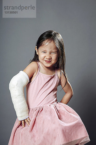 Porträt eines niedlichen Mädchens stehend mit Händen auf der Hüfte vor grauem Hintergrund