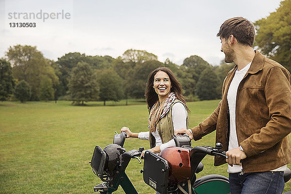 Glückliches Paar unterhält sich beim Spaziergang mit Fahrrädern im Park