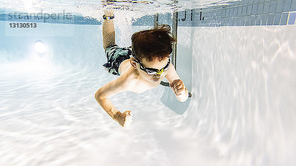 Süßer Junge ohne Shirt  der im Pool unter Wasser schwimmt