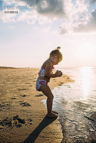 Glückliches Mädchen spielt mit Sand am Strand gegen den Himmel