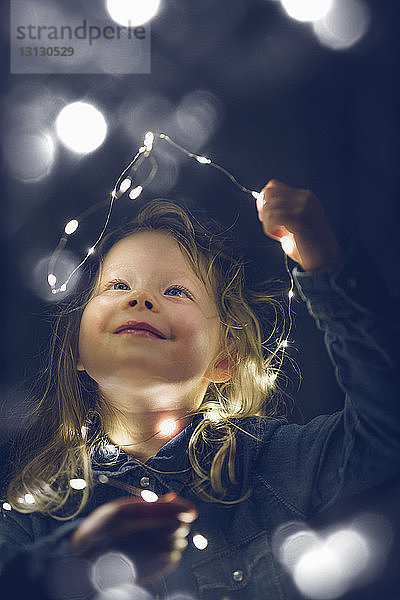 Fröhliches Mädchen spielt nachts mit beleuchteten Lichterketten