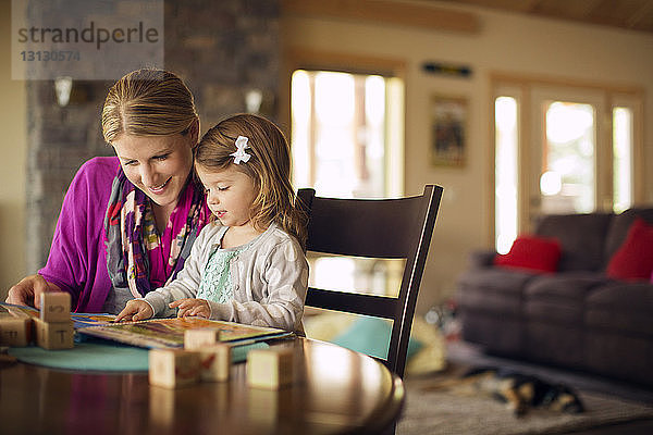 Mutter und Tochter schauen sich zu Hause ein Buch auf dem Tisch an