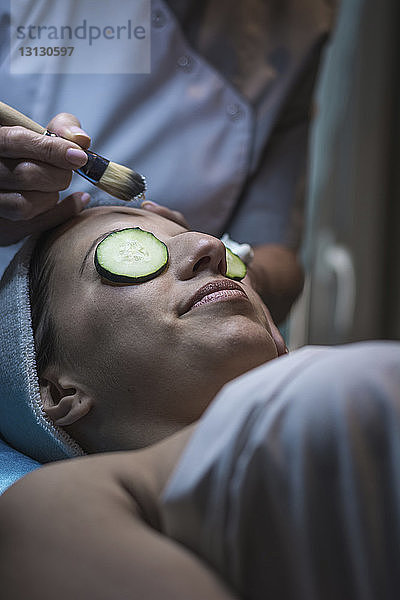 Mittelteil einer Kosmetikerin  die einer Kundin im ästhetischen Zentrum eine Gesichtsmaske aufsetzt