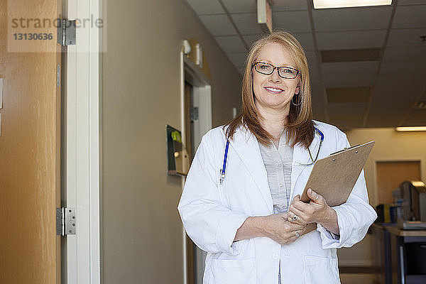 Porträt einer Ärztin mit Klemmbrett im Krankenhauskorridor stehend