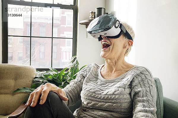 Ältere Frau trägt einen Virtual-Reality-Simulator  während sie auf einem Sofa sitzt