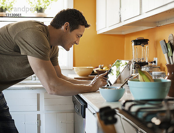 Lächelnder Mann benutzt Tablette  während er zu Hause in der Küche steht