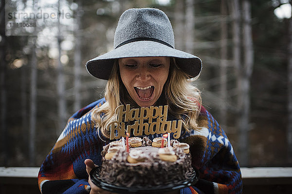 Fröhliche Frau hält Geburtstagskuchen  während sie im Winter im Freien steht