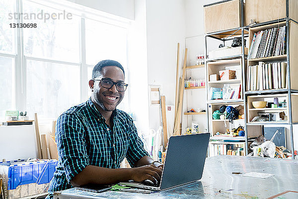 Porträt eines glücklichen Geschäftsmannes  der am Laptop im Büro arbeitet