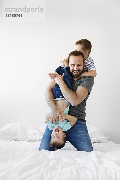 Fröhlicher Vater spielt zu Hause mit Söhnen im Bett an der Wand