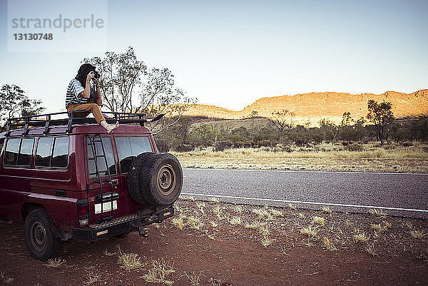 Frau fotografiert auf dem Autodach in der Wüste