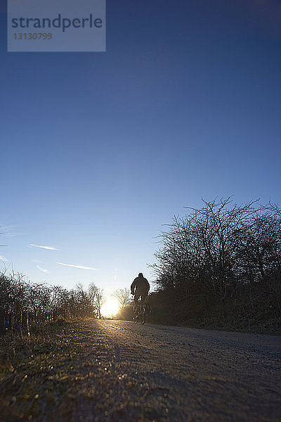 Oberflächenniveau einer Frau mit Silhouette  die auf einem Fußweg Fahrrad fährt  vor blauem Himmel bei Sonnenuntergang