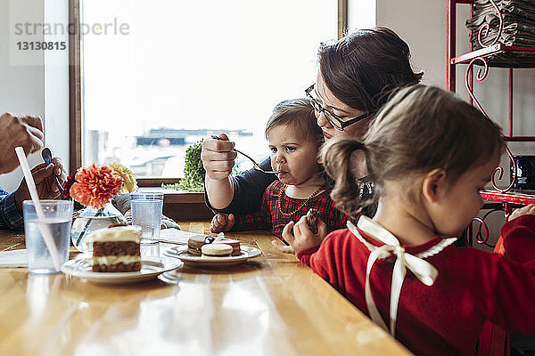 Mutter füttert Mädchen  während sie mit der Familie am Restauranttisch sitzt