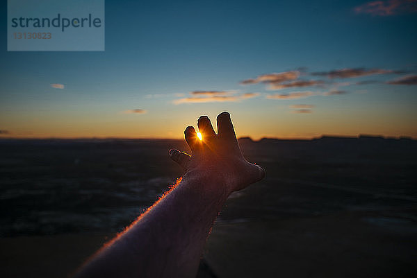 Abgehackte Hand eines Mannes  der bei Sonnenuntergang über die Silhouette der Landschaft gegen den Himmel gestikuliert