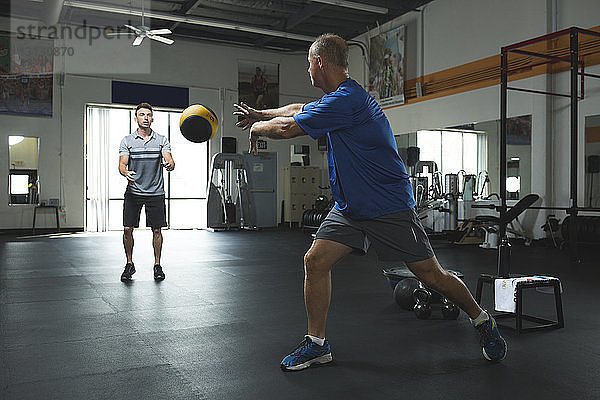 Kunde gibt Fitnessball an Trainer ab  während er im Fitnessstudio trainiert