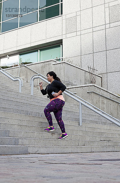 Seitenansicht einer Frau  die Musik hört  während sie auf Stufen in der Stadt übt