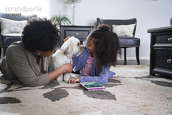 Mutter und Tochter spielen mit Lhasa Apso  während sie zu Hause auf dem Teppich liegen