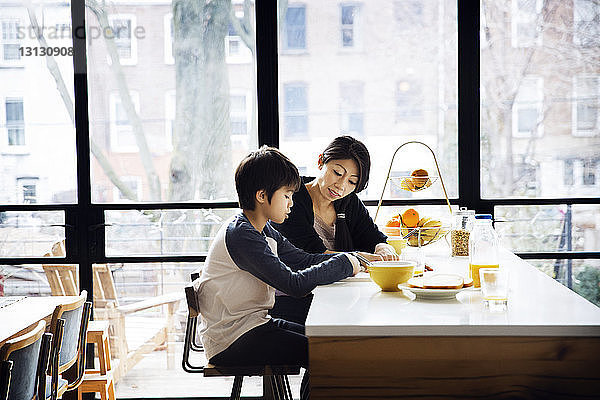 Mutter unterrichtet Sohn auf Tisch gegen Fenster zu Hause