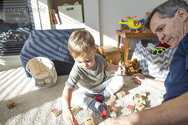 Großvater und Enkel spielen zu Hause im Wohnzimmer mit Spielzeugklötzen
