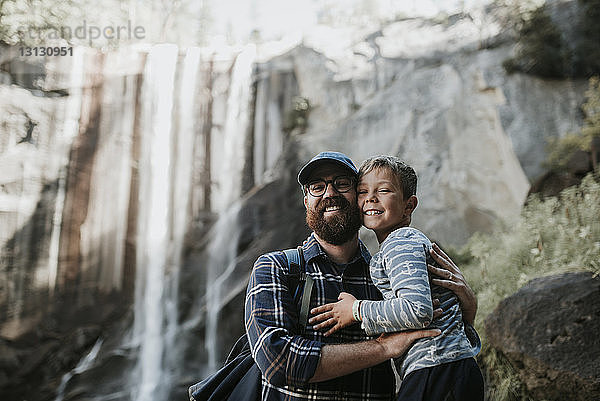 Porträt von fröhlichem Vater und Sohn vor Wasserfall im Yosemite-Nationalpark