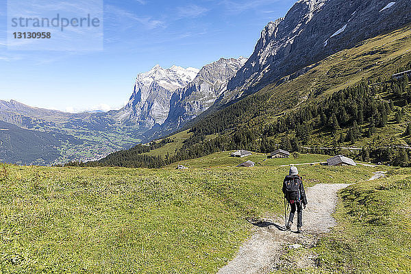 Rückansicht einer Wanderin  die auf einem Wanderweg durch die Berge geht