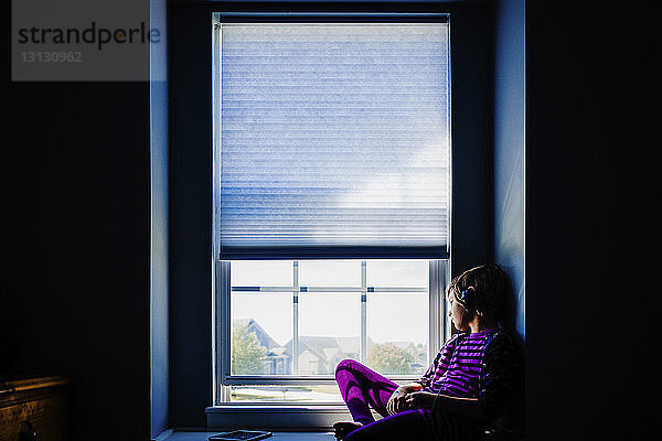 Mädchen hört Musik  während sie zu Hause durchs Fenster schaut