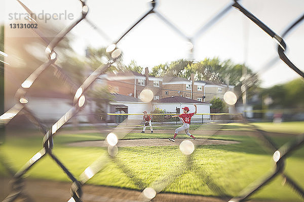 Baseballspieler wirft den Ball auf dem Spielfeld in voller Länge durch den Maschendrahtzaun