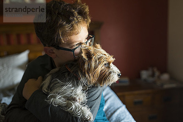 Junge mit Hund schaut weg  während er zu Hause auf dem Bett sitzt