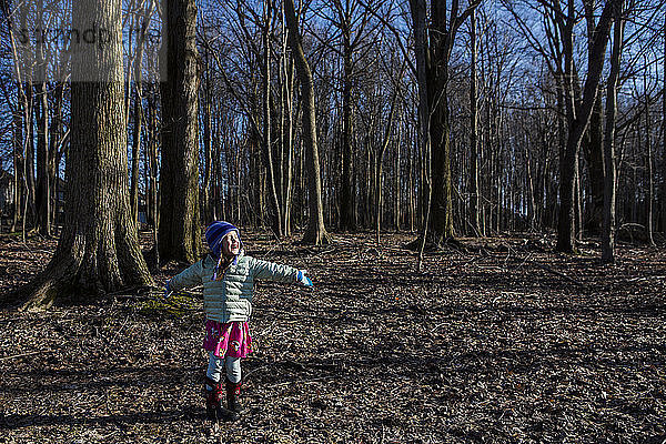 Glückliches Mädchen mit ausgestreckten Armen auf einem Feld im Wald stehend