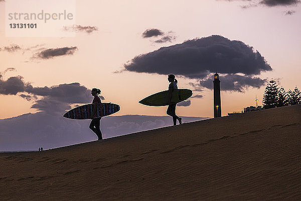 Scherenschnittfreunde mit Surfbrettern bei Sonnenuntergang in der Wüste vor bewölktem Himmel