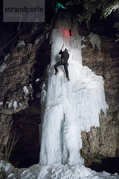 Niedrigwinkelansicht eines Eiskletterers  der auf einen gefrorenen Wasserfall klettert