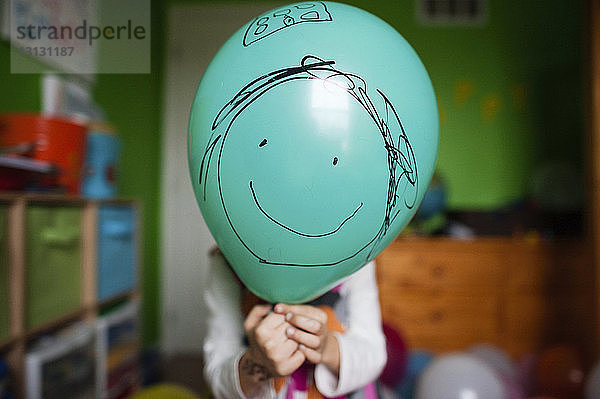 Mädchen hält Ballon mit Smiley zu Hause