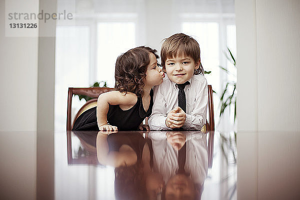 Süßes Mädchen küsst Bruder am Tisch sitzend