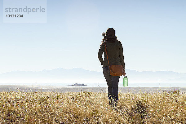 Rückansicht einer Frau  die auf einem Grasfeld gegen den klaren Himmel auf Antelope Island läuft