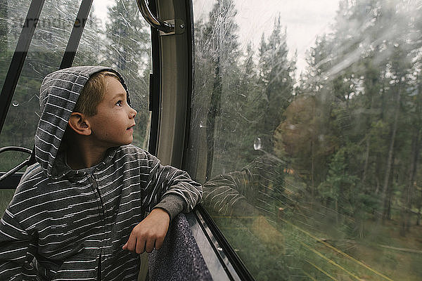 Junge schaut durch ein Fenster  während er in einer Luftseilbahn fährt