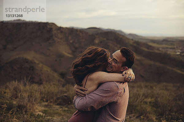 Seitenansicht eines liebenden jungen Paares  das sich auf dem Feld gegen Berge umarmt