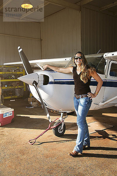 Porträt einer selbstbewussten Frau  die am Hangar an einem Propellerflugzeug steht