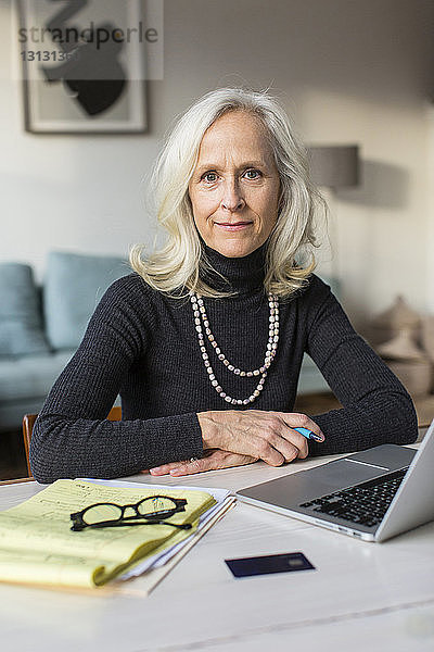 Porträt einer selbstbewussten älteren Frau mit Laptop-Computer auf dem Tisch zu Hause