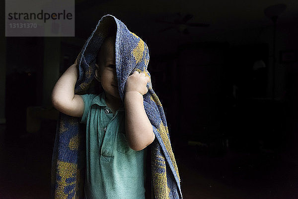 Porträt eines süßen kleinen Jungen  der mit einem Handtuch spielt  während er zu Hause in der Dunkelkammer steht