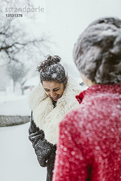Fröhliche Freundinnen stehen bei Schneefall auf dem Feld