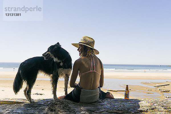 Rückansicht einer glücklichen Frau mit Hund am Strand