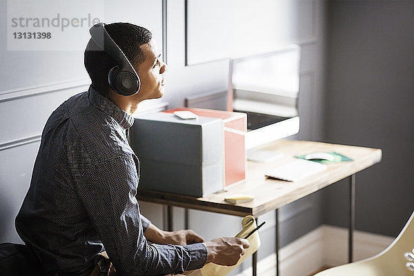 Geschäftsmann schaut weg  während er im Büro Musik hört