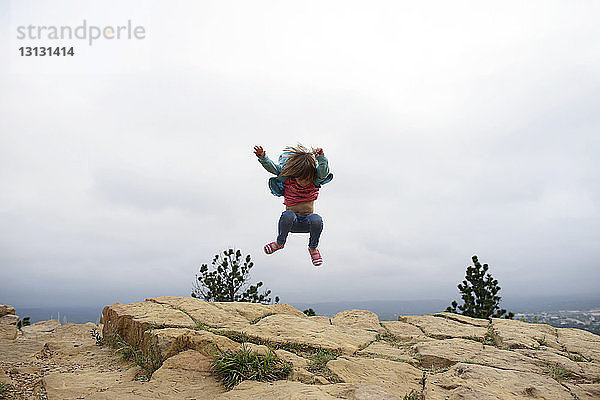 Mädchen in voller Länge springt im Custer State Park auf Bergfelsen gegen den Himmel