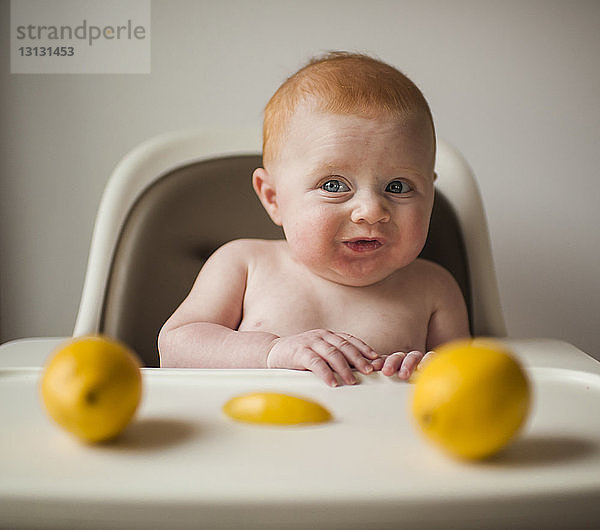 Junge ohne Hemd macht Gesicht  während er auf einem Hochstuhl sitzt  mit Zitronen im Vordergrund