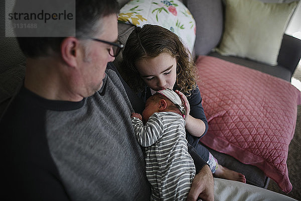 Schrägaufnahme eines Mädchens  das seine Schwester küsst und vom Vater zu Hause auf dem Sofa getragen wird