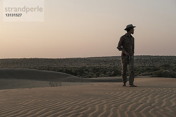Mann schaut weg  während er bei Sonnenuntergang in der Thar-Wüste vor dem klaren Himmel steht
