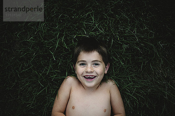 Portrait eines fröhlichen Jungen  der auf einem Grasfeld im Hinterhof liegt