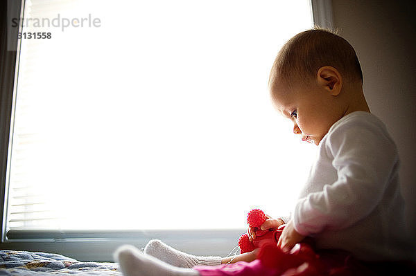 Kleines Mädchen spielt mit Spielzeug  während es zu Hause am Fenster sitzt